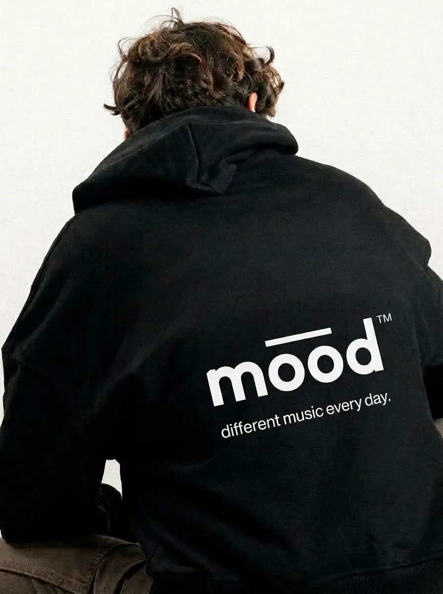 Espalda de un buzo negro con capucha: logo mood grande en blanco y debajo «different music every day.»